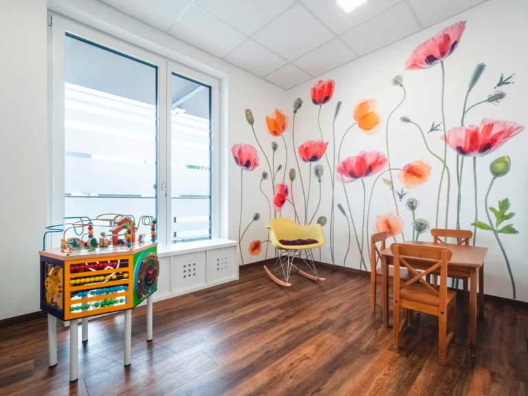 Warteraum mit Blumentapete, Schaukelstuhl und Spieltisch.